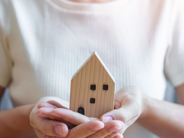 Person holding a small wooden house model in cupped hands.