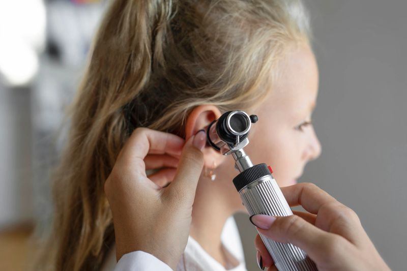 Doctor examining girl's ear with otoscope