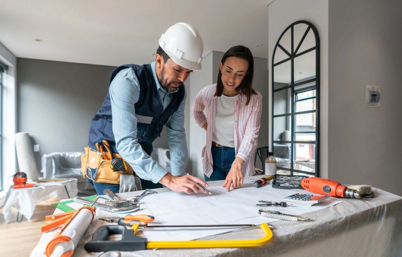 Woman remodeling her house and talking to the contractor while looking at the blueprints