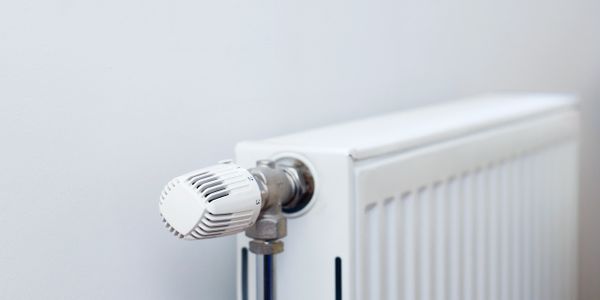 Close-up of a white radiator thermostat valve attached to a radiator.
