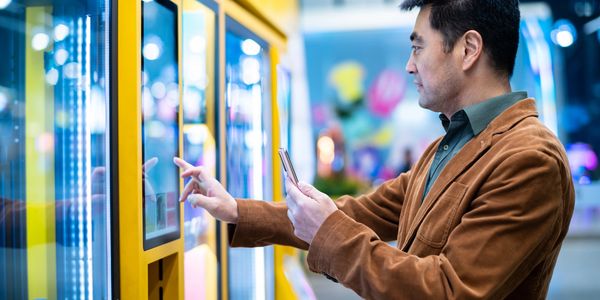 Man using touchscreen kiosk while holding a smartphone.