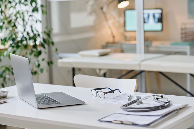 Close-up of workplace of doctor with laptop and medical card on table at office