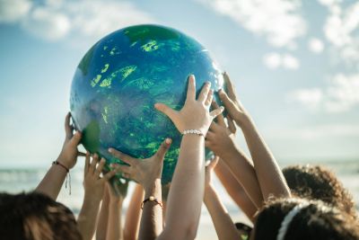 Multiple hands holding a globe against the sky.