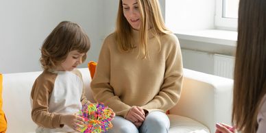 A child playing with a colorful toy during a therapy session with a woman and a therapist.