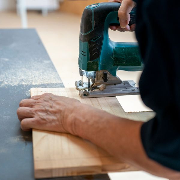 Person using a jigsaw to cut a wooden board on a workbench.