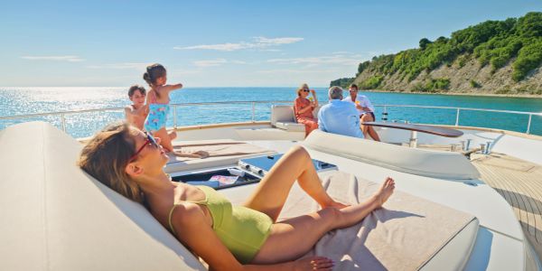 People relaxing on a yacht near a green shoreline.