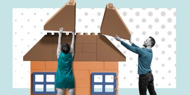 Two people assembling a large toy house with oversized blocks.