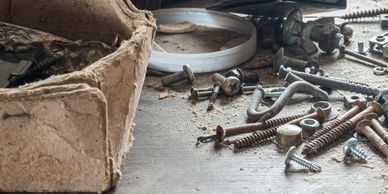 A collection of rusty screws, bolts, and nuts on a dusty wooden surface.