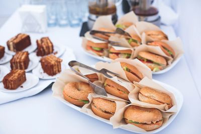Tray of bagel sandwiches and plates of chocolate cake slices on a white table.