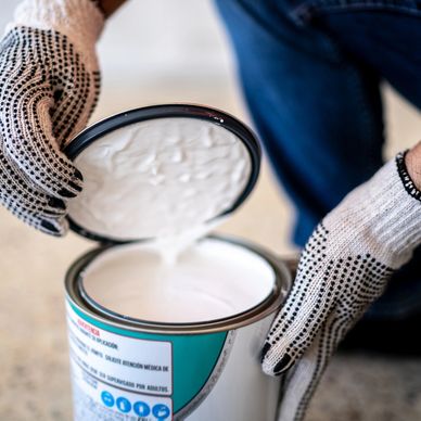Person opening a can of white paint wearing gloves.