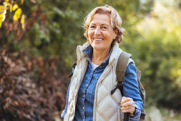 Smiling older woman hiking outdoors with backpack and trekking pole.