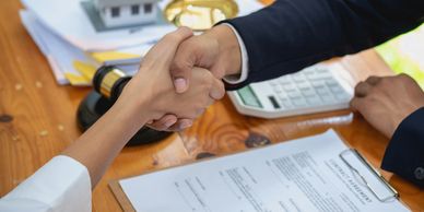 Business handshake over a signed contract on a wooden desk.