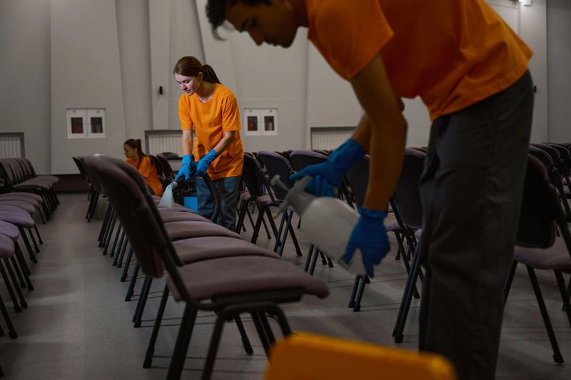 Professional team of cleaners working together on sanitizing the sitting area of the hall