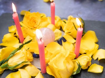 Yellow roses and pink candles arranged with a rose quartz crystal.