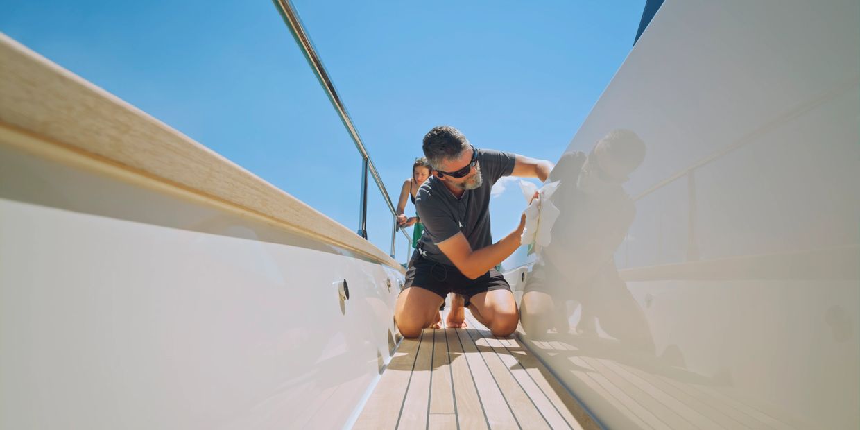 Man cleaning a yacht deck on a sunny day.