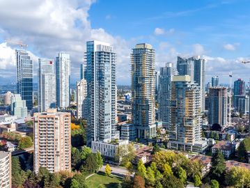 A city skyline with modern high-rise buildings and construction cranes under a blue sky.