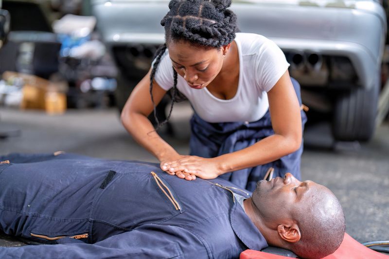 Mechanical guy at car repair shop got accident lay on the floor mechanical girl first aid life saving by perform cardiopulmonary resuscitation CPR before the medic come