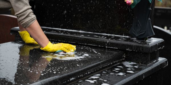 Person cleaning a black granite gravestone with yellow gloves and soap.