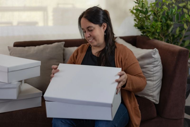 A young lady opening a surprise gift in a large white box, sitting on an armchair in the living room.