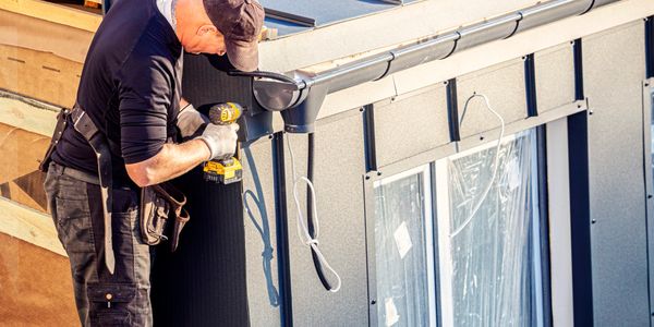 Worker using a drill to install siding on a house exterior.