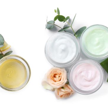 Three jars of pastel-colored creams with flowers and leaves on white.