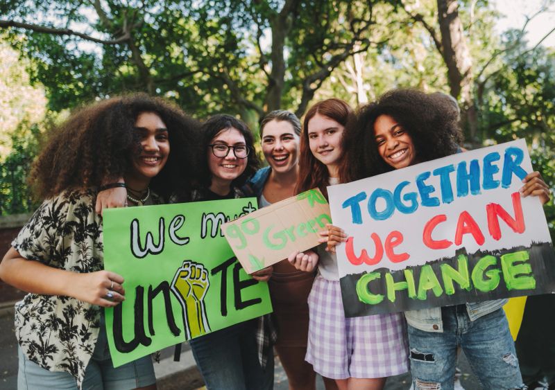 Multicultural teenage activists smiling at the camera while holding posters and placards during a peaceful protest. Group of generation z demonstrators campaigning for environmental change and unity.