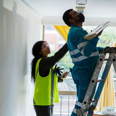 Two workers inspecting a ceiling with one on a ladder and the other assisting.