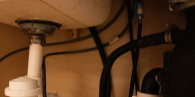 Plumbing pipes and hoses under a sink with wooden background.