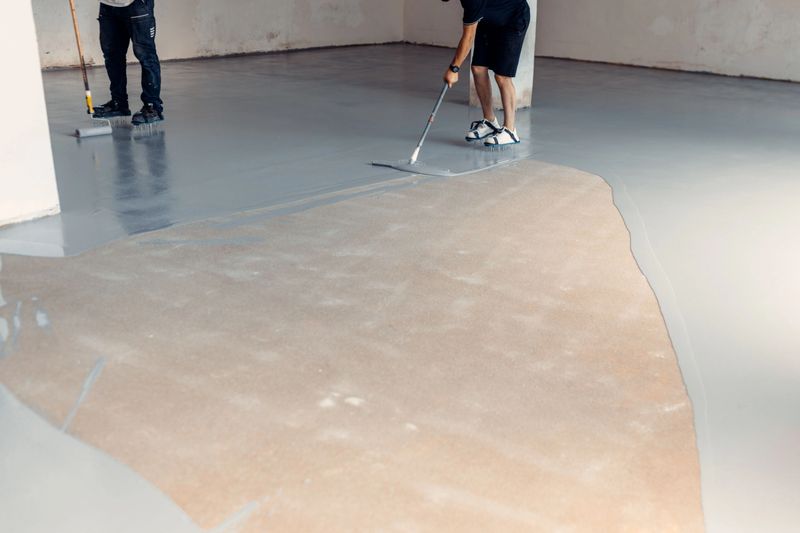 Two construction workers applying grey epoxy resin in an industrial hall