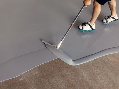 Person applying gray epoxy floor coating.