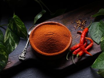 A bowl of red chili powder with fresh red chilies on a wooden board.