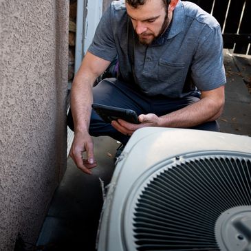 Technician inspecting an outdoor air conditioning unit with a tablet.