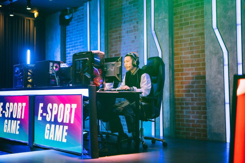 Team of Asian teenage sport gamers play in multiplayer PC Game on eSport tournament and celebrating success  raising hands up and give-five to each other during winner esports league tournament in gaming station.