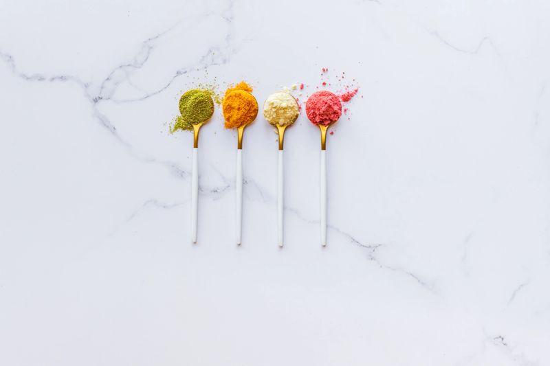 Lime, Grapefruit, Strawberry and Pineapple powders in teaspoons on marble surface with copy