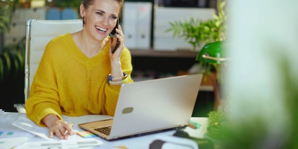 Woman in yellow sweater talking on phone at desk.