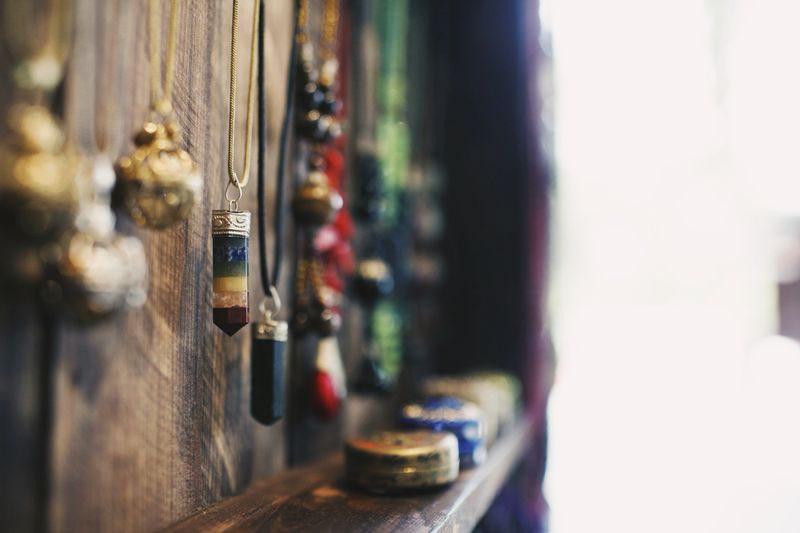 A closeup of crystal necklaces hanging on a wooden surface under the lights with a blurry background