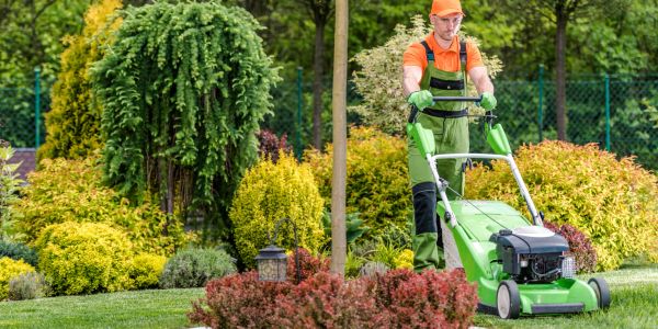 Man mowing lawn with green lawn mower.