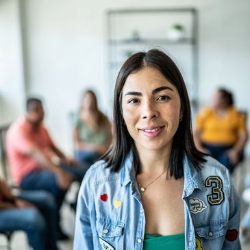 Smiling woman in focus with group therapy session in the background.