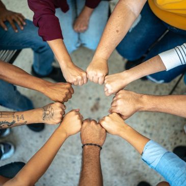 Diverse group of people joining fists in a circle symbolizing unity.