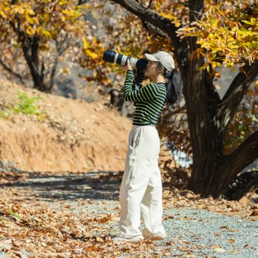 A woman in autumn scenery taking photos with a DSLR camera.
