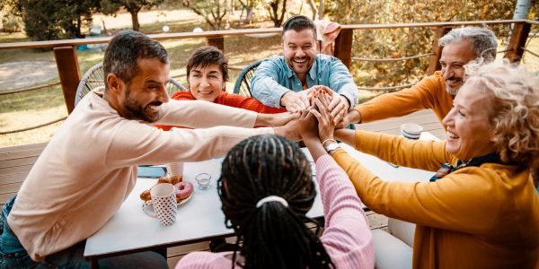 A group of friends joining hands in a cheerful gesture around a table outdoors.