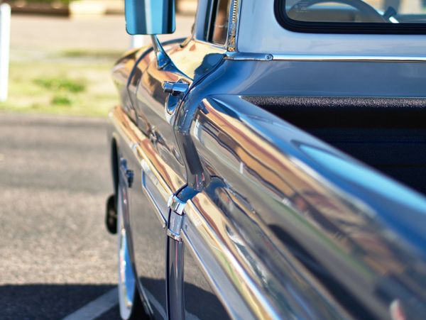 Close-up of a shiny blue vintage pickup truck's side and mirror.