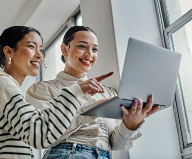 Two women smiling and looking at a laptop together.