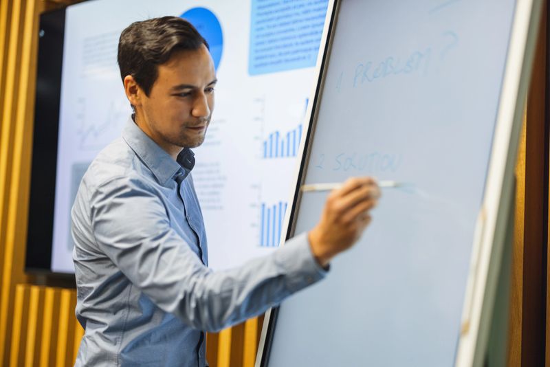 Confident young Asian male researcher and manager explaining his ideas during a business meeting. He is drawing on a white board.