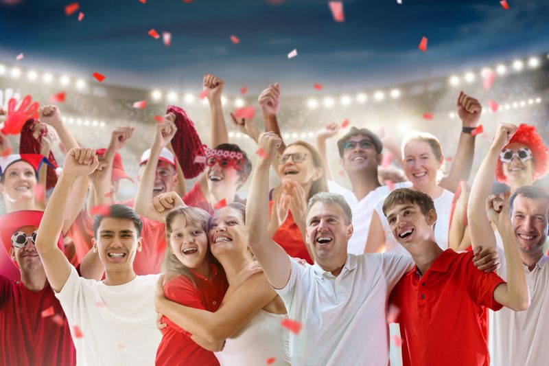 Football supporter on stadium in red and white shirt. Happy fans on soccer pitch watching winning team play. Group of supporters with flag and jersey cheering excited. Championship game. Victory party
