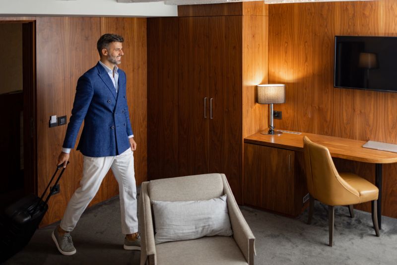 Smiling middle-aged man carring luggage, wearing blue suit coat and white pants