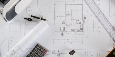 Architectural blueprints with drafting tools, calculator, and model house on a workspace.
