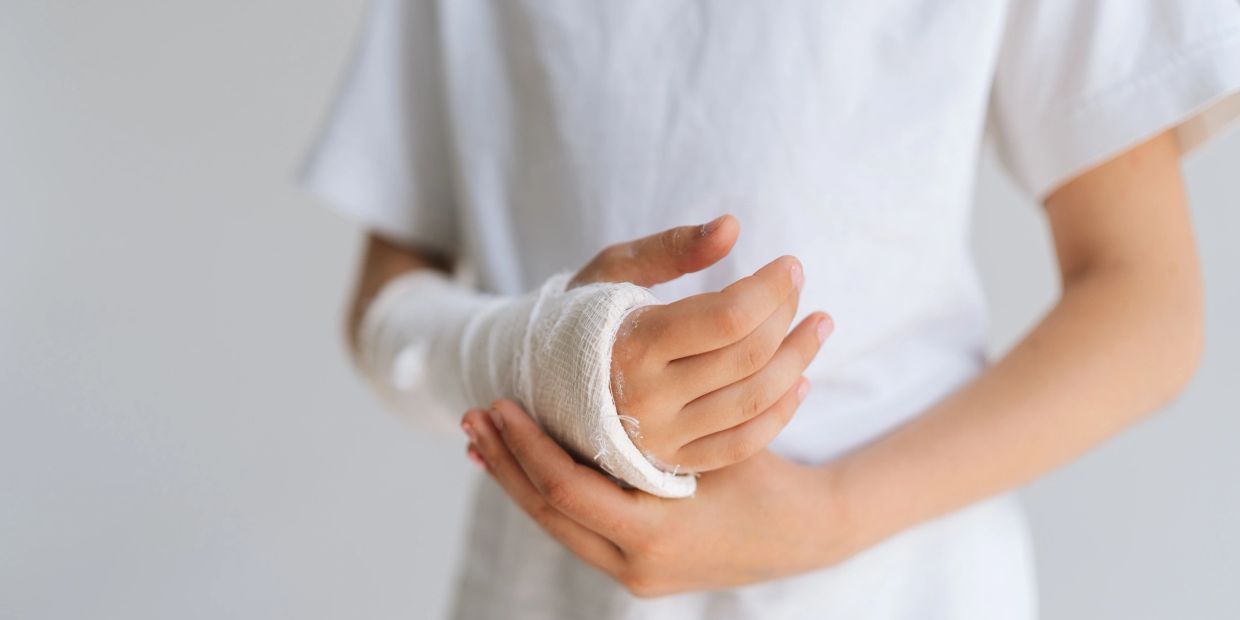 Child with bandaged hand wearing a white shirt.