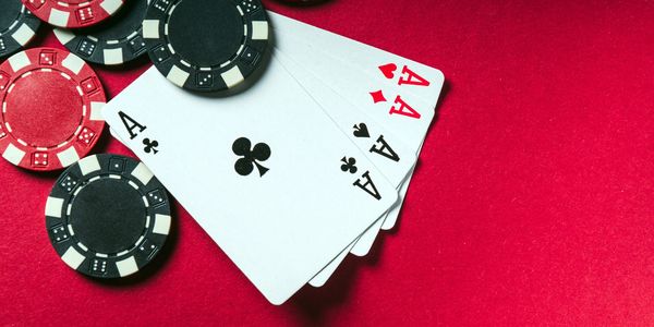 Four aces with poker chips on a red surface.