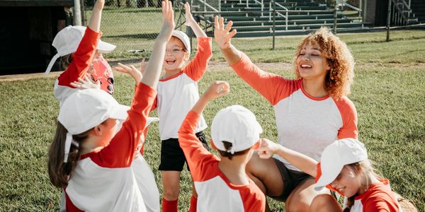 Youth baseball team celebrating a victory with their coach outdoors.